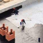 Two workers conduct waterproofing of the roof with bitumen. View from above.