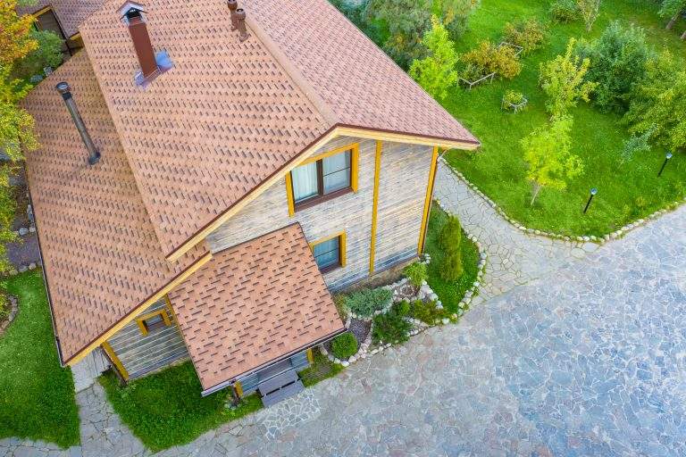 Top view of the two-storey cottage. The roof is made of flexible tiles. Modern construction technologies. Landscape design of the site. Paths at the house are made of stone. Rest in the countryside.