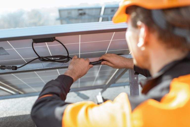 Electrician connecting wires of solar panels on a rooftop photovoltaic power plant. Concept of installing solar stations