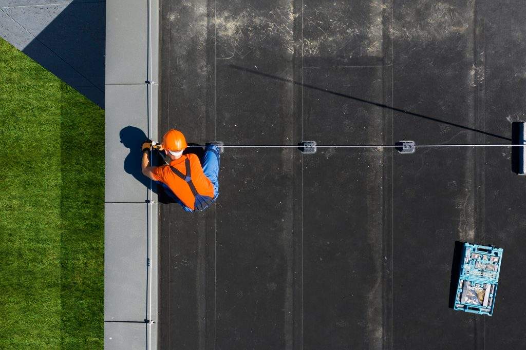 Caucasian Technician Wearing Orange Uniform and Hard Hat Installing Lightning Protection System Rod on Top of Commercial Building. Protect Structure From Elements.