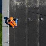 Caucasian Technician Wearing Orange Uniform and Hard Hat Installing Lightning Protection System Rod on Top of Commercial Building. Protect Structure From Elements.