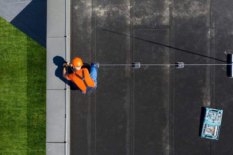 Caucasian Technician Wearing Orange Uniform and Hard Hat Installing Lightning Protection System Rod on Top of Commercial Building. Protect Structure From Elements.