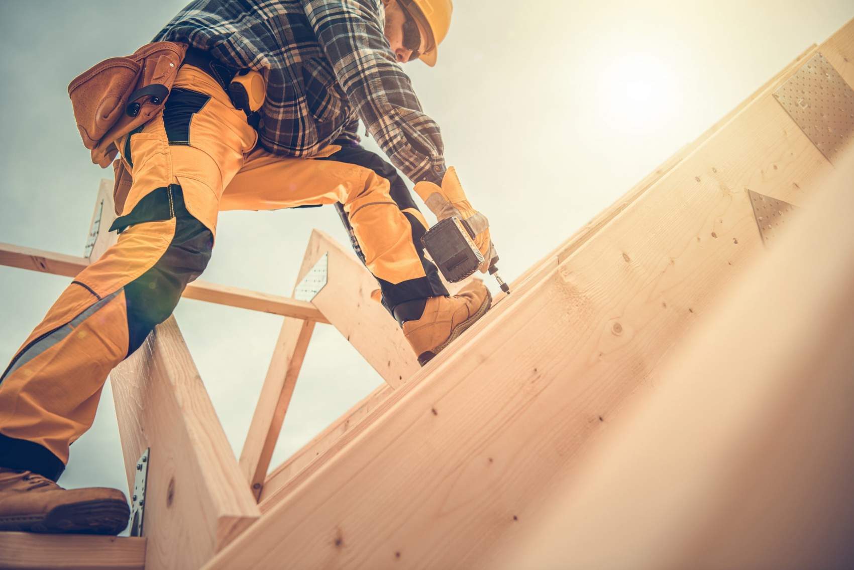 Caucasian Contractor Worker in His 40s with Drill Driver in His Hand. Carpenter Working on Wooden House Skeleton Frame Roof Section. Construction Industry Theme.