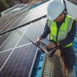 Electric engineer working white safety on height building, installing solar panels on the rooftop working using notebook computer, inspecting, measuring, collecting data for repairing