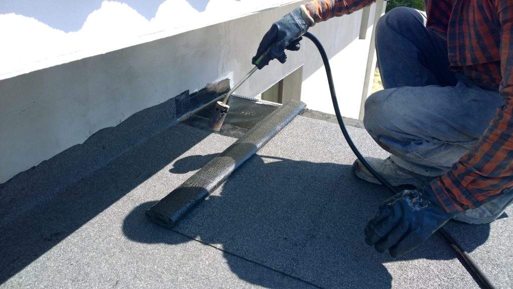 Roofer preparing part of bitumen roofing felt roll for melting by gas heater torch flame
