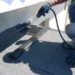 Roofer preparing part of bitumen roofing felt roll for melting by gas heater torch flame